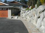 Pavers edging an asphalt driveway with a granite boulder wall